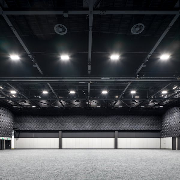 A spacious, modern event hall with a textured black wall and bright overhead lights illuminating the empty carpeted floor.